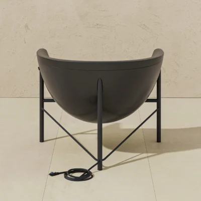 Modern black bowl chair on a metal stand placed on beige tiled floor; a coiled power cord lies in front.