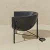 0002_GJ_KosmosChair2_Profile_.RGB_color.0010_1440x Black curved bowl chair on a metal frame sits on a beige tiled floor; a coiled power cord lies nearby on the floor.