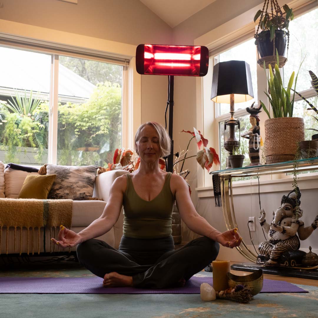A woman sitting on a yoga mat indoors with a Heliosa 66 Black Heater behind her