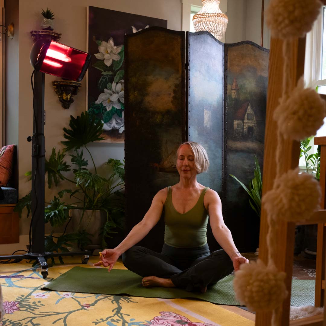 A woman sitting on a yoga mat indoors with a Heliosa 66 Black Heater behind her